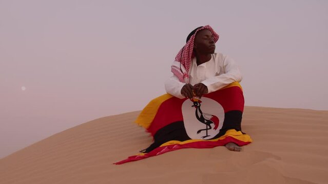 African young man holding flag of Uganda in desert