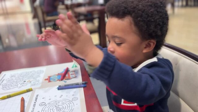 Funny 3 year-old exotic black toddler playing with crayons seated inside a cafeteria