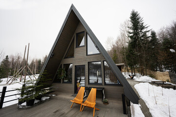 Terrace of wooden triangle country tiny cabin house in mountains and two chairs. - obrazy, fototapety, plakaty