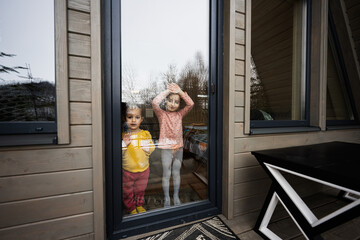 Two sisters looks throw the glass door on terrace of wooden country tiny cabin house.