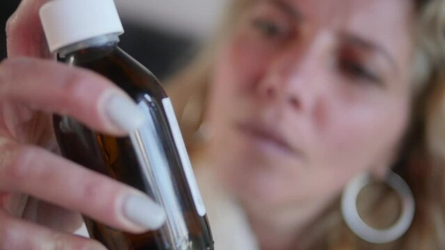 An ill woman shakes up liquid medicine in the bottle.