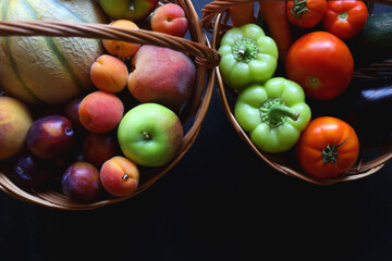 Two wicker baskets with healthy seasonal fruit and vegetable. Dark background, top view.