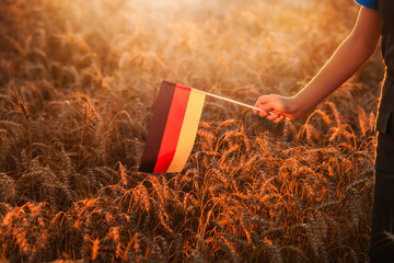 Small Germany flag in female hand at sunset in wheat field.