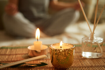 Close-up of scented candle, diffuser. A woman sits in a lotus position, meditates.