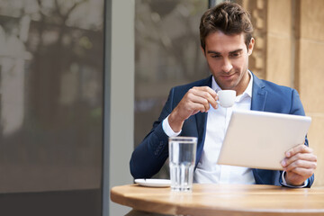 Reading online with an expresso. a young businessman sitting at an outdoor cafe using a digital...