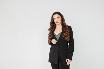 young businesswoman with long curly hair in a black suit stands on a white background