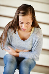 Feeling the emptiness grow inside. an unhappy young woman sitting on a staircase holding her stomach.