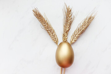 Spikelets of wheat and a golden Easter egg lie on a white background