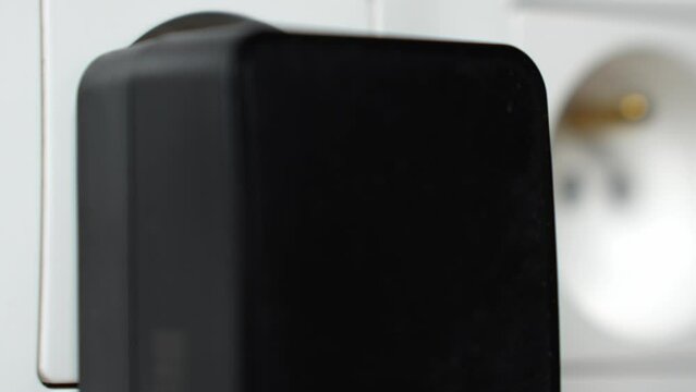 Hand connects black plug into electrical socket. Plugging electronic device to the electrical network