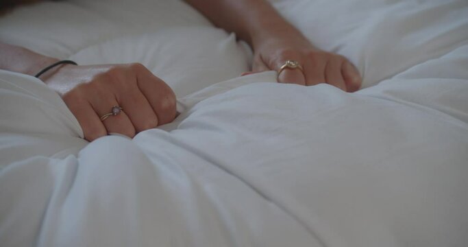 Womans hands gripping white bed sheet tightly. Sex concept. Close up, static