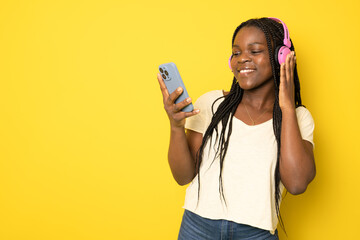 Smiling african woman listening music and using smartphone over yellow background