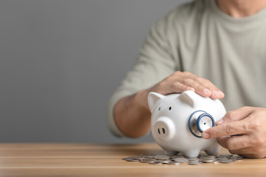 Financial health check, The idea of ​​taking care of saving money, Man using stethoscope to check white piggy bank on desk with grey copy space. Health and finance concept