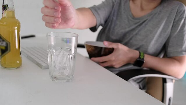 The girl is going to drink beer, throws ice into a glass standing on a white computer table, next to a bottle of beer and a keyboard