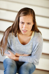 Fototapeta premium First cut is the deepest. Portrait of an unhappy young woman sitting on a staircase holding her stomach.