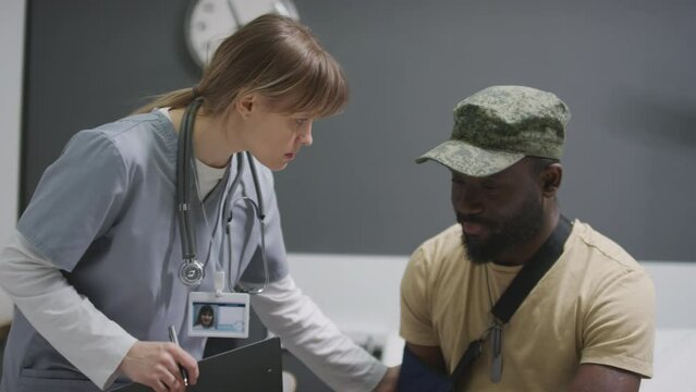 Doctor working in military hospital giving recommendations to serviceman with broken arm before discharge