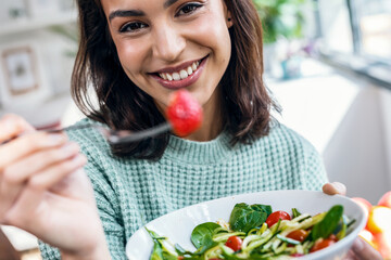 Beautiful smiling woman eating healthy salad while sitting on the table at home.