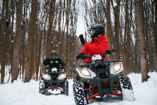 Man is looking behind at his friend. Two people are riding ATV in the winter forest