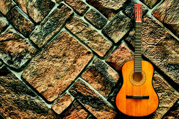 Yellow orange acoustic guitar on gray brown dark brick wall