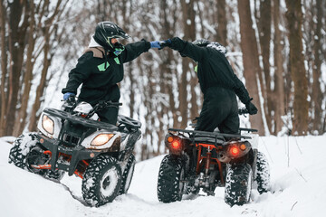 Making gestures. Two people are riding ATV in the winter forest