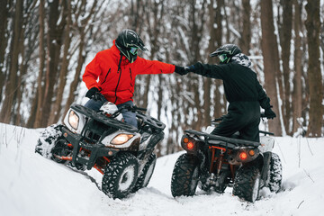 Fototapeta na wymiar Knocking the fists. Two people are riding ATV in the winter forest