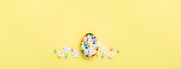 Easter Eggs with Sweets and Spring Flowers on Yellow Background
