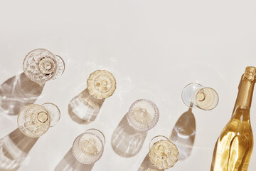 Summer party drinks flat lay, wine glasses with white sparkling wine and sunshine shadow on light table. Minimal pattern with beautiful wine glasses, above view still life, beige golden color