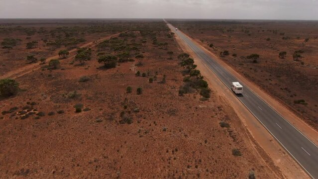 Aerial view of camper van on empty road in Australia surrounded by red desert during cloudy day