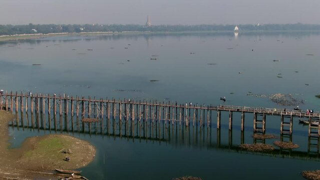 Local residents walking over the wooden U-Bein Bridge in Myanmar. Drone lowering tilt shot