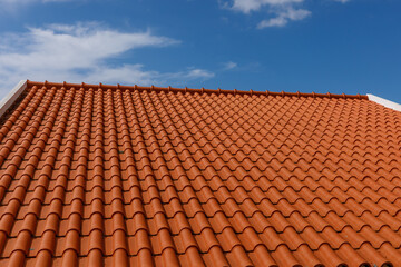 Red tiles panels roof under blue sky.