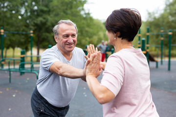 Fototapeta premium Friendly family couple doing gymnastic exercises together in summer city park