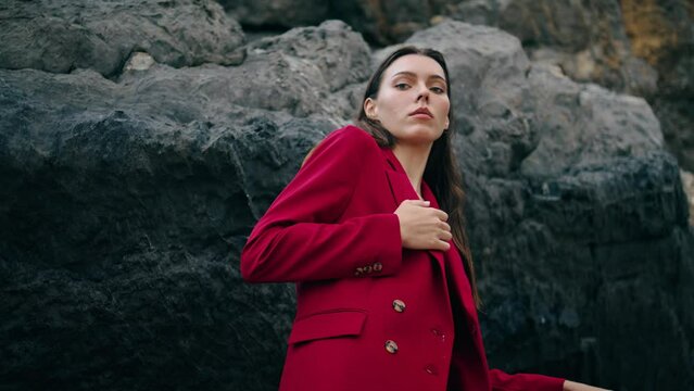 Confident girl standing mountains in red suit close up. Woman posing on rock.
