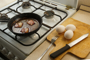 Lard is fried in a frying pan, and next to it, chicken eggs lie on a cutting board. Cooking scrambled eggs with lard.