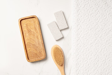 Flat lay cosmetic body care product presentation scene made with empty wooden tray, white towel, pumice stone and scrubbing brush.