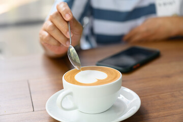 Close up woman hand and white coffee cup with heart shape latte art menu on wooden background in the cafe.