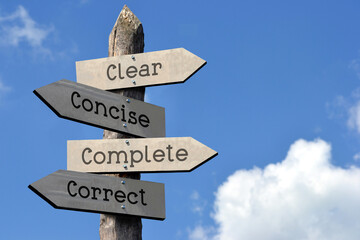 Clear, concise, complete, correct - wooden signpost with four arrows, sky with clouds
