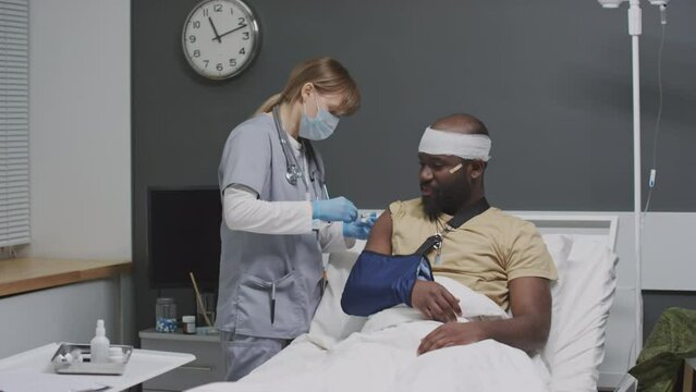 African American Soldier With Bandage Around His Head And Broken Arm Getting Injection In His Shoulder