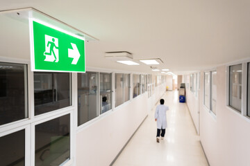 Selective fire exit sign on white ceiling.Green fire escape sign hang on the ceiling in the...