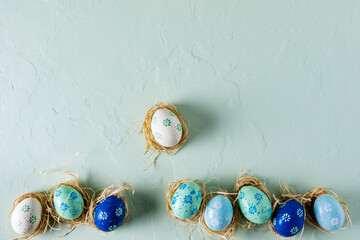 Row of hand painted Easter eggs on light green concrete background. Flat lay, top view with copy space