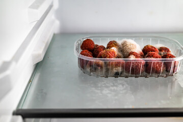 Moldy raspberries in a plastic basket inside a refrigerator. Food past its expiration date, spoiled...