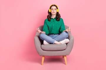 Full size photo of restful girl dressed green shirt sit on armchair in meditation pose listen relaxed music isolated on pink background