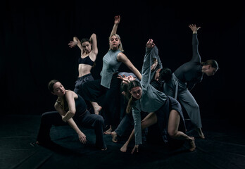Group of young people, man and woman making artistic performance, dancing against black studio...