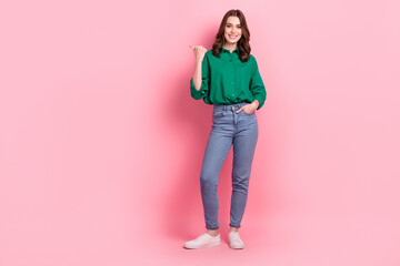 Full length photo of funny cute lady dressed green blouse pointing thumb emtpy space isolated pink color background