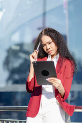 Cheerful african american woman holding digital tablet standing outdoors in front of modern business building