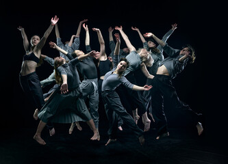 Group of young people in gray stage costumes making performance, dancing against black studio...