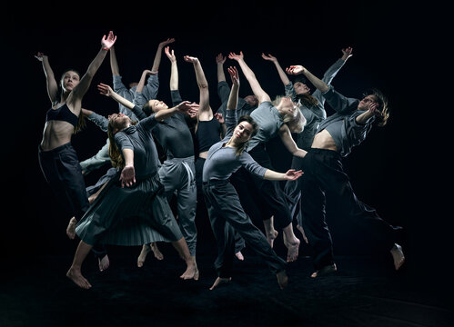 Group of young people in gray stage costumes making performance, dancing against black studio background. Concept of modern freestyle dance, contemporary art, movements, hobby and creative lifestyle