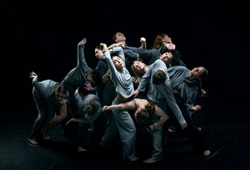 Group of young people in gray stage costumes making performance, dancing against black studio...