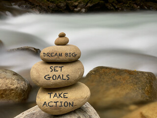Inspirational quote concept - dream big set goals take action text on pebbles background. Stock photo.