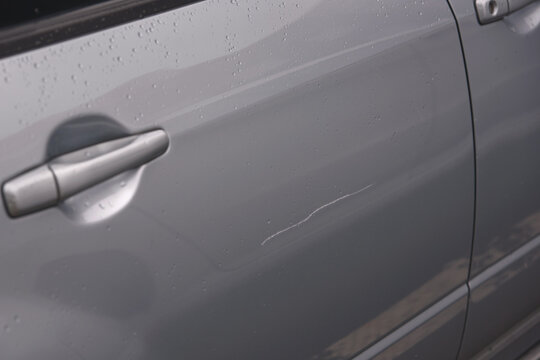 Сar door scratched, damage to paint and lacquer coat. Dent car scratch. Vandal scratched car with nail at parking lot. .