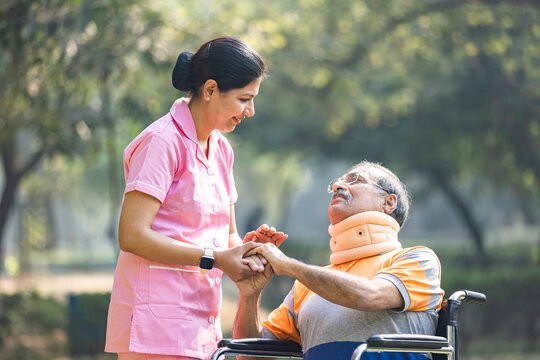Nurse talking to male senior patient on wheelchair with a neck brace at the park. - Powered by Adobe