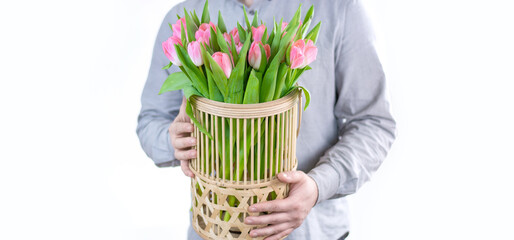 A man holds a basket with a bouquet of flowers in his hands on a white background. Gift, flower delivery, greeting card. spring tulips